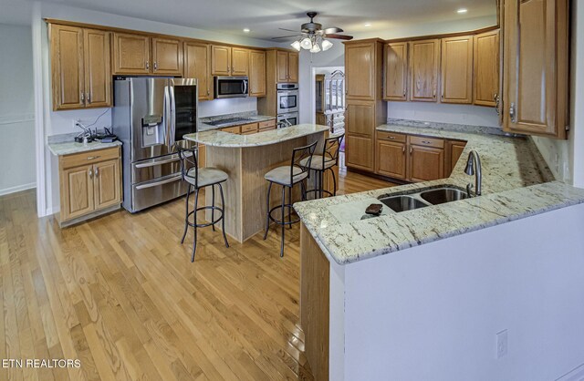 kitchen featuring a breakfast bar area, light wood-style flooring, a center island, appliances with stainless steel finishes, and light stone countertops