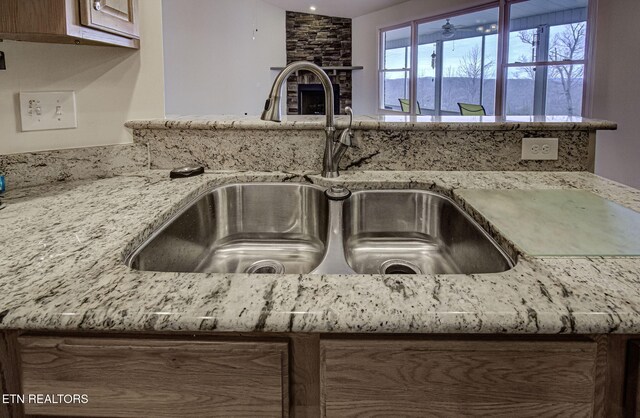 interior details with light stone countertops, a sink, and a stone fireplace