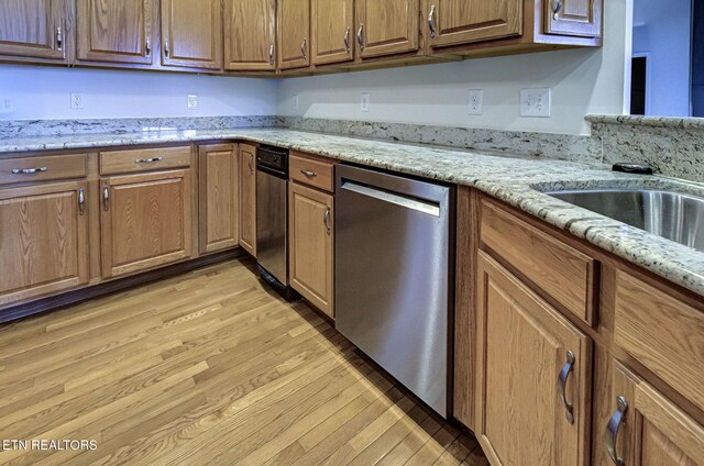 kitchen with dishwasher, light stone counters, light wood-style flooring, and brown cabinets