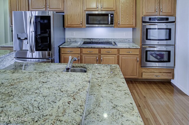 kitchen with brown cabinetry, appliances with stainless steel finishes, light stone countertops, light wood-style floors, and a sink