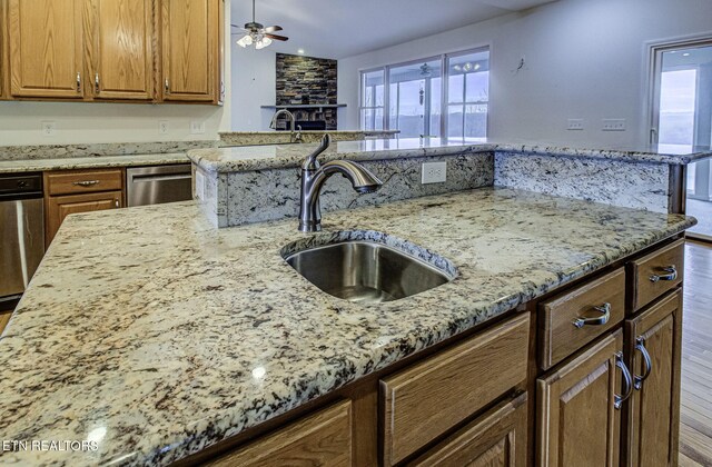 kitchen featuring light stone counters, brown cabinetry, a sink, and dishwasher