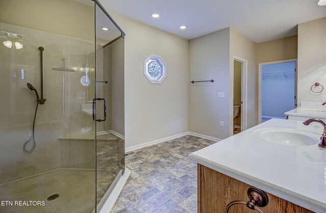 full bath with toilet, two vanities, a sink, baseboards, and a stall shower