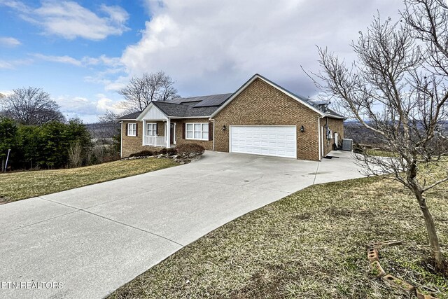 ranch-style house featuring a garage, concrete driveway, cooling unit, roof mounted solar panels, and brick siding