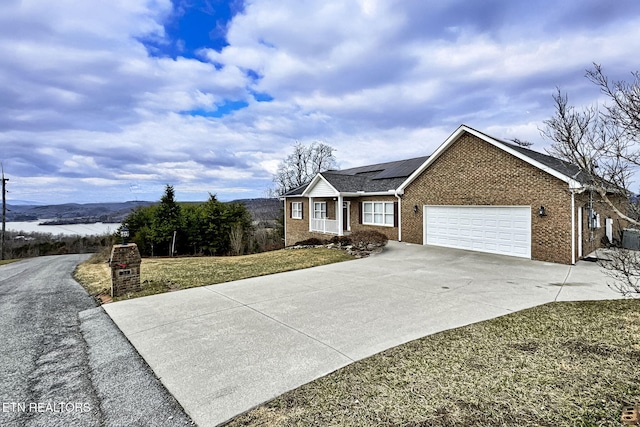 ranch-style house with a mountain view, a garage, brick siding, driveway, and roof mounted solar panels