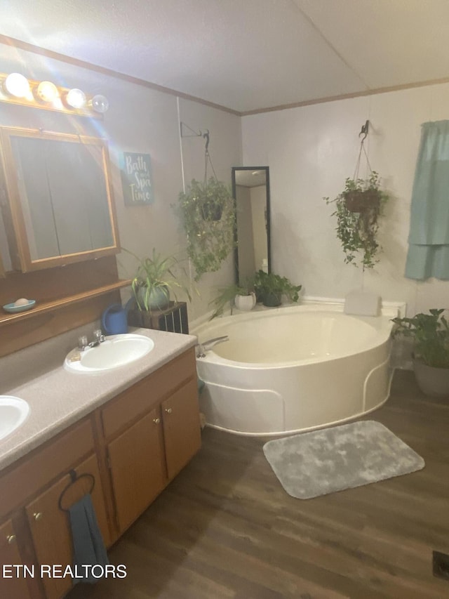 full bathroom featuring double vanity, a garden tub, a sink, and wood finished floors