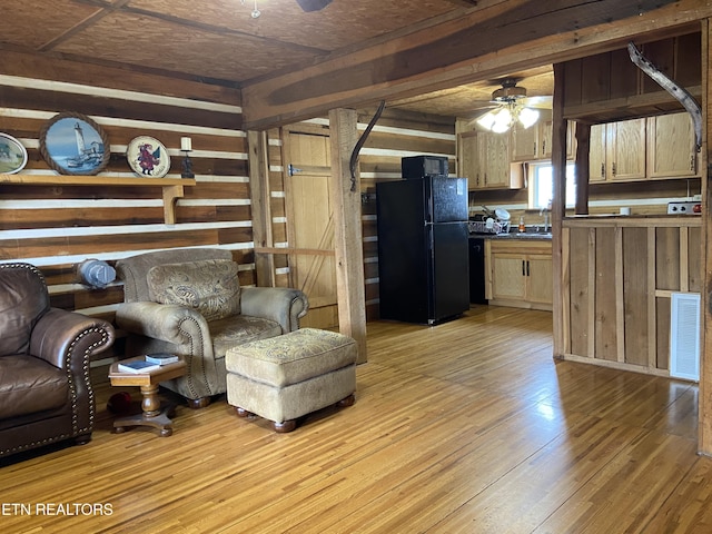 living room featuring wood walls, ceiling fan, visible vents, and light wood-style flooring