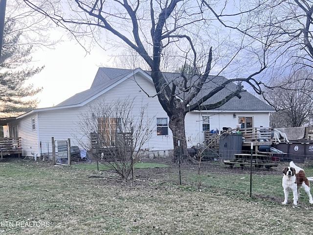 back of house featuring a shingled roof, a lawn, and a wooden deck