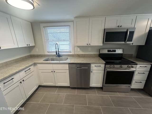 kitchen featuring appliances with stainless steel finishes, white cabinetry, a sink, light stone countertops, and dark tile patterned floors