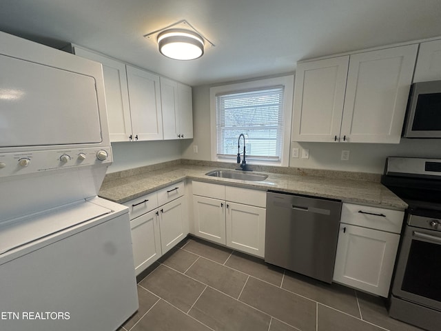 kitchen featuring stainless steel appliances, dark tile patterned floors, a sink, white cabinets, and stacked washing maching and dryer