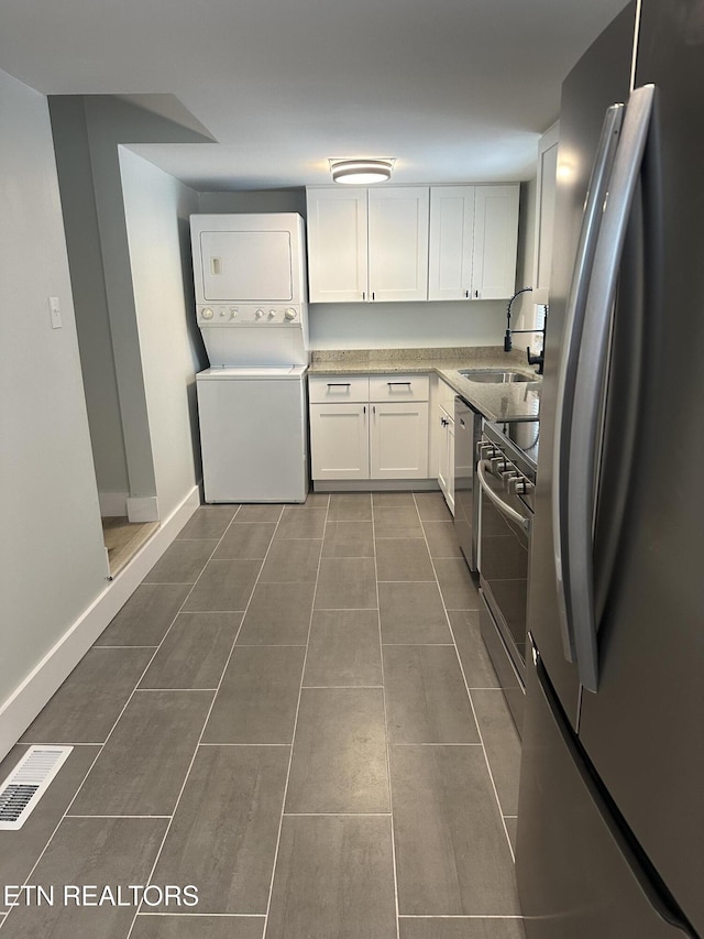 kitchen with stainless steel appliances, a sink, stacked washer / drying machine, white cabinets, and light countertops