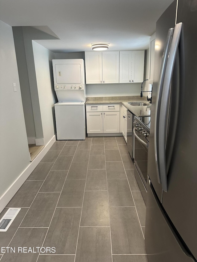 kitchen with a sink, white cabinetry, light countertops, appliances with stainless steel finishes, and stacked washing maching and dryer