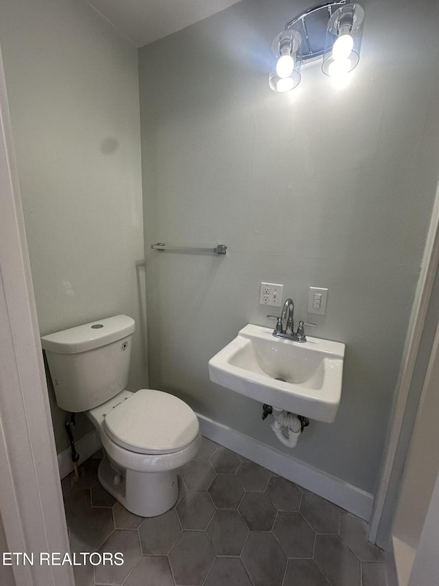 half bathroom featuring tile patterned flooring, a sink, toilet, and baseboards