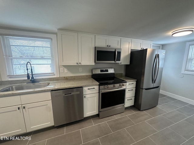 kitchen with appliances with stainless steel finishes, tile patterned flooring, white cabinets, and a sink