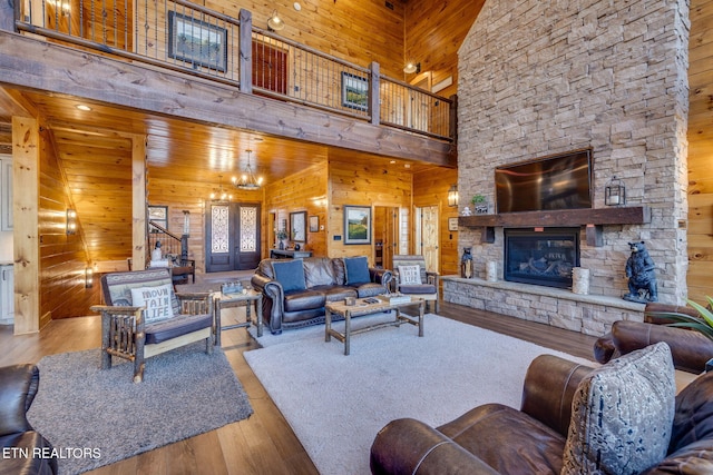 living room with stairway, a towering ceiling, a stone fireplace, wooden walls, and wood finished floors