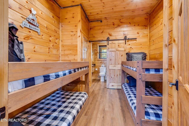 bedroom featuring wood finished floors, wood ceiling, wooden walls, and a barn door