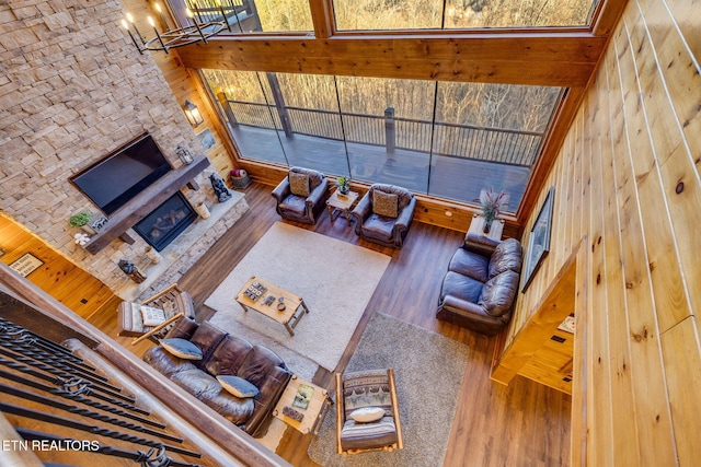 living area featuring a stone fireplace, a high ceiling, wood finished floors, and a notable chandelier