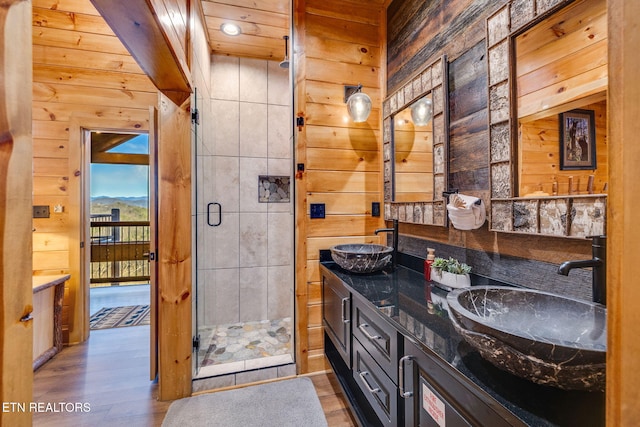 full bath with wood walls, wood finished floors, a sink, and a stall shower