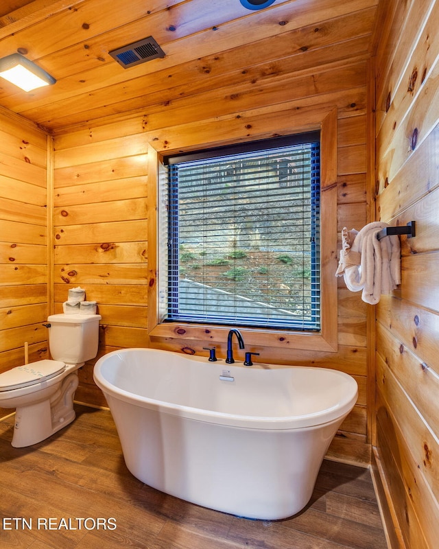 full bathroom with toilet, wood walls, a freestanding bath, and wood finished floors