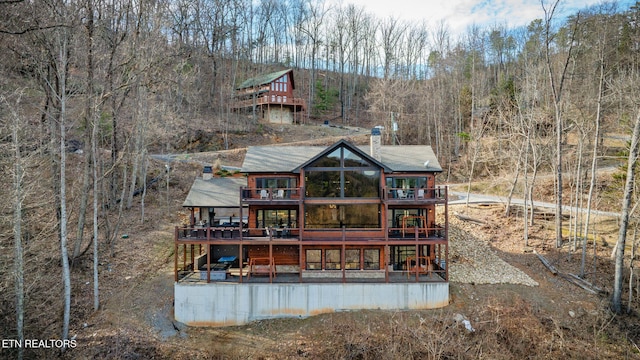 rear view of property featuring a wooded view, a chimney, and a wooden deck