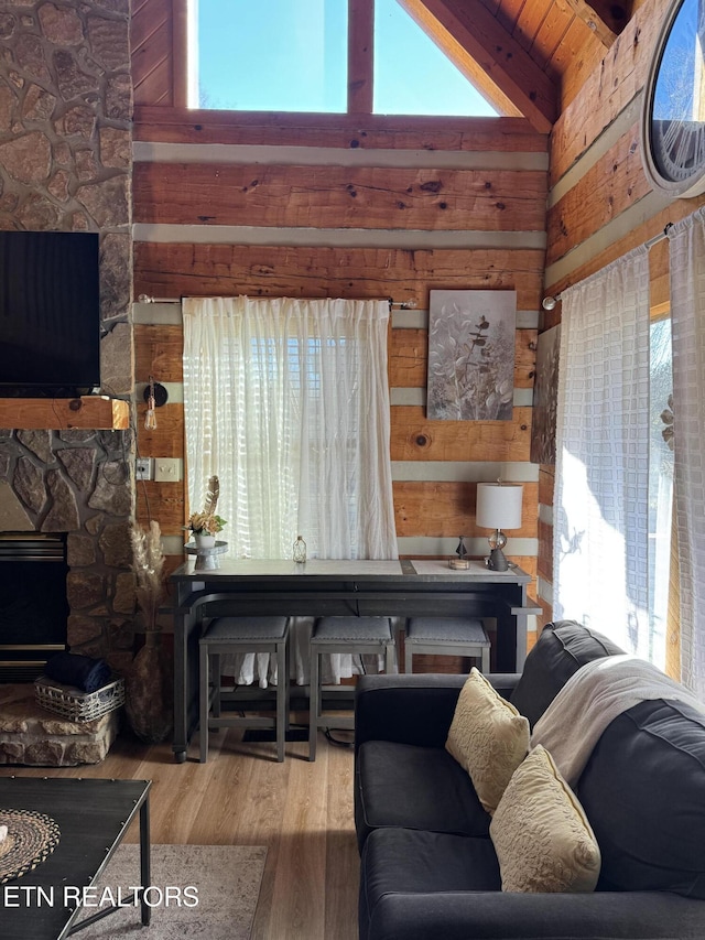 living room with a wealth of natural light, wooden walls, wood finished floors, and a stone fireplace