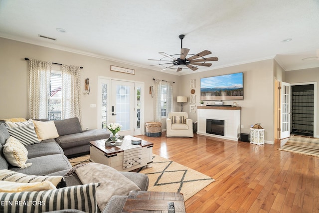 living room featuring crown molding, a glass covered fireplace, visible vents, and light wood-style floors