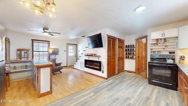 kitchen with electric range, a glass covered fireplace, light wood-style flooring, and white cabinets