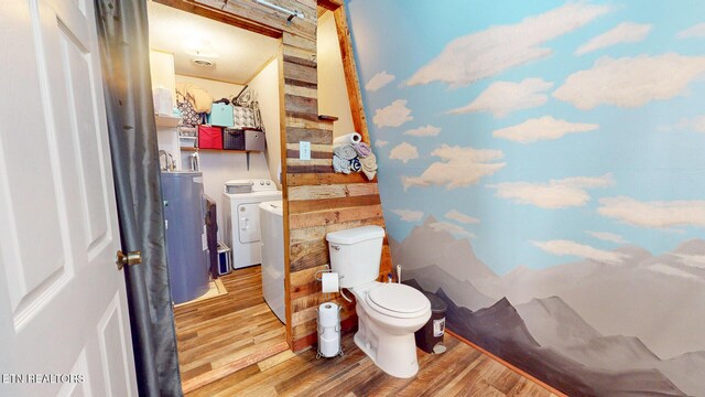 half bath featuring washer and dryer, electric water heater, toilet, and wood finished floors