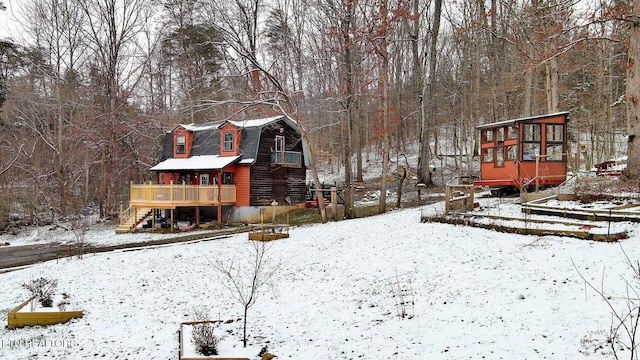 snow covered back of property with stairway, a deck, and a gambrel roof