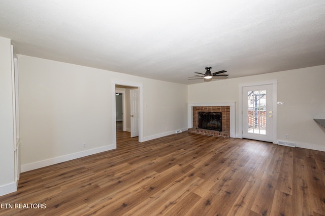 unfurnished living room with ceiling fan, hardwood / wood-style flooring, visible vents, baseboards, and a brick fireplace