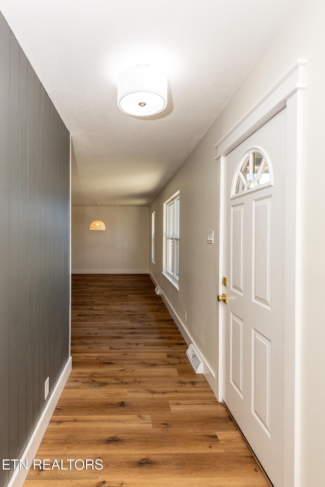 corridor with visible vents, wood walls, light wood-style flooring, and baseboards