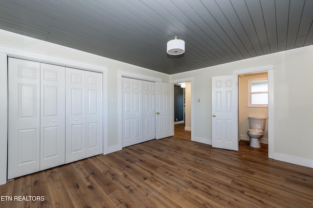 unfurnished bedroom with wood ceiling, baseboards, dark wood finished floors, and two closets