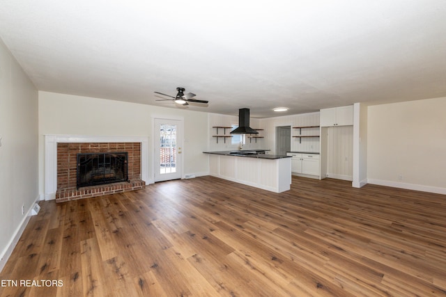 unfurnished living room featuring a brick fireplace, a ceiling fan, baseboards, and wood finished floors