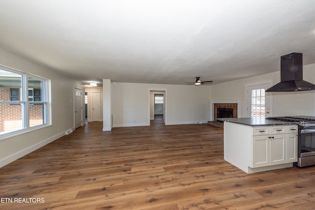 kitchen with island range hood, dark countertops, open floor plan, a fireplace, and stainless steel range with gas stovetop