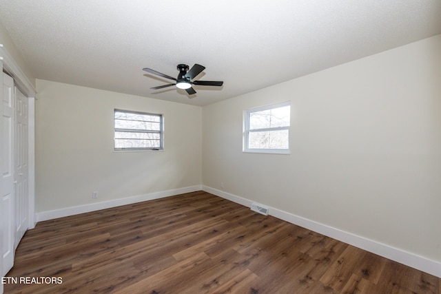 spare room featuring baseboards, dark wood finished floors, visible vents, and a healthy amount of sunlight