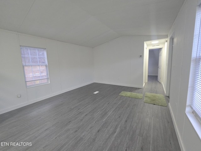 unfurnished room featuring lofted ceiling, dark wood-style flooring, and a decorative wall