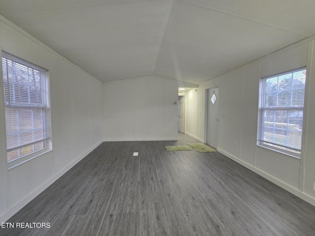 unfurnished room featuring baseboards, vaulted ceiling, dark wood-type flooring, and a decorative wall