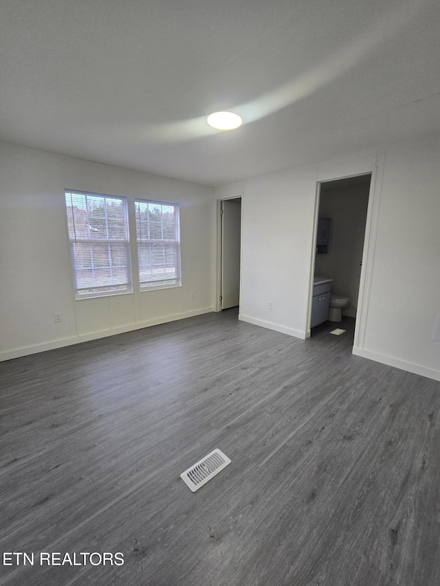 interior space with dark wood-style flooring, visible vents, baseboards, and ensuite bathroom