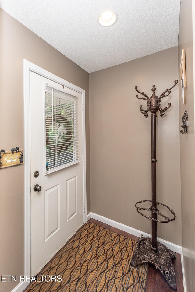 doorway to outside with dark wood finished floors, a textured ceiling, and baseboards