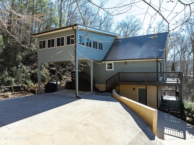 back of property with a carport, concrete driveway, metal roof, and stairs