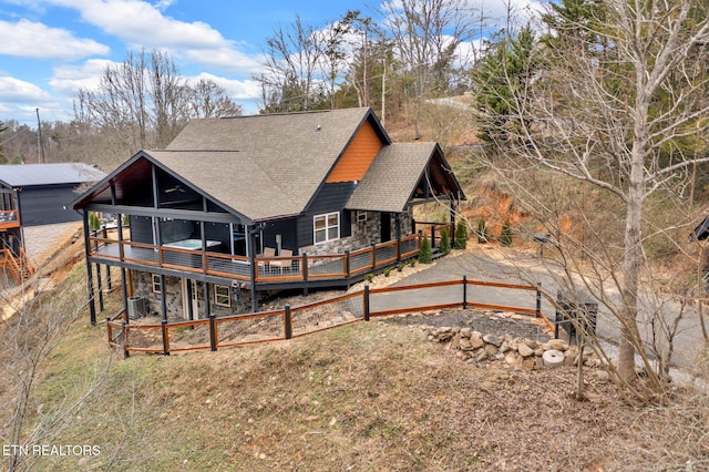 rear view of property featuring a shingled roof, cooling unit, stone siding, and a wooden deck