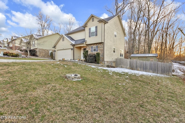 traditional home featuring an outdoor fire pit, an attached garage, fence, stone siding, and a front lawn