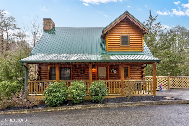 log cabin with covered porch, metal roof, a chimney, and log siding