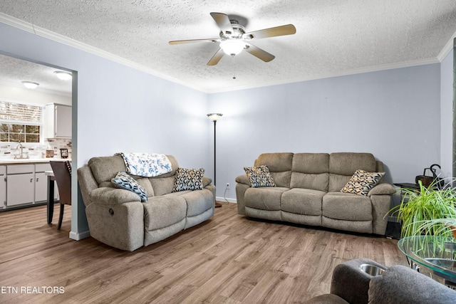 living room featuring light wood-style floors, a textured ceiling, a ceiling fan, and crown molding