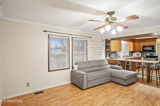 living room featuring light wood-style flooring, crown molding, visible vents, and a ceiling fan