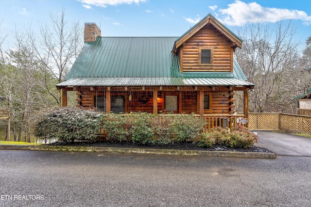 log home with metal roof, a porch, log siding, and aphalt driveway