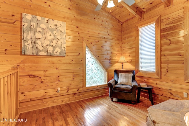 living area with vaulted ceiling with beams, ceiling fan, wooden walls, wood finished floors, and wood ceiling