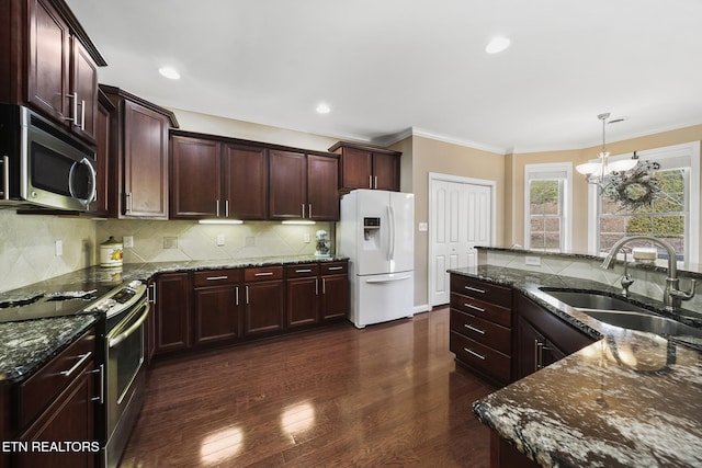 kitchen featuring stainless steel appliances, dark wood-type flooring, a sink, hanging light fixtures, and dark stone countertops