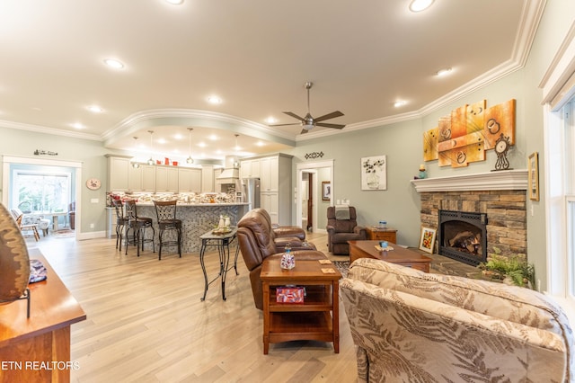 living room featuring ceiling fan, a stone fireplace, ornamental molding, and light wood-style flooring