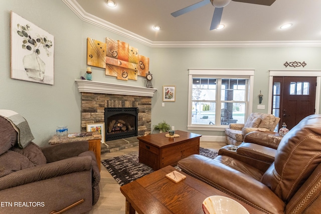 living room with light wood-style flooring, ceiling fan, crown molding, a stone fireplace, and recessed lighting