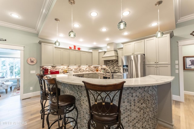 kitchen with light stone counters, a breakfast bar area, custom exhaust hood, pendant lighting, and high end fridge